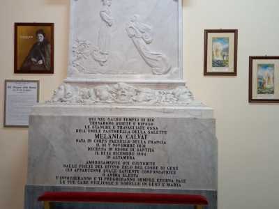 Si presenta come una lapide in marmo composta da un'alta base su cui poggia il quadrifondo di un bassorilievo: rappresenta l'apparizione della Madonna della Salette accanto alla figura di Melanie che la segue con lo sguardo